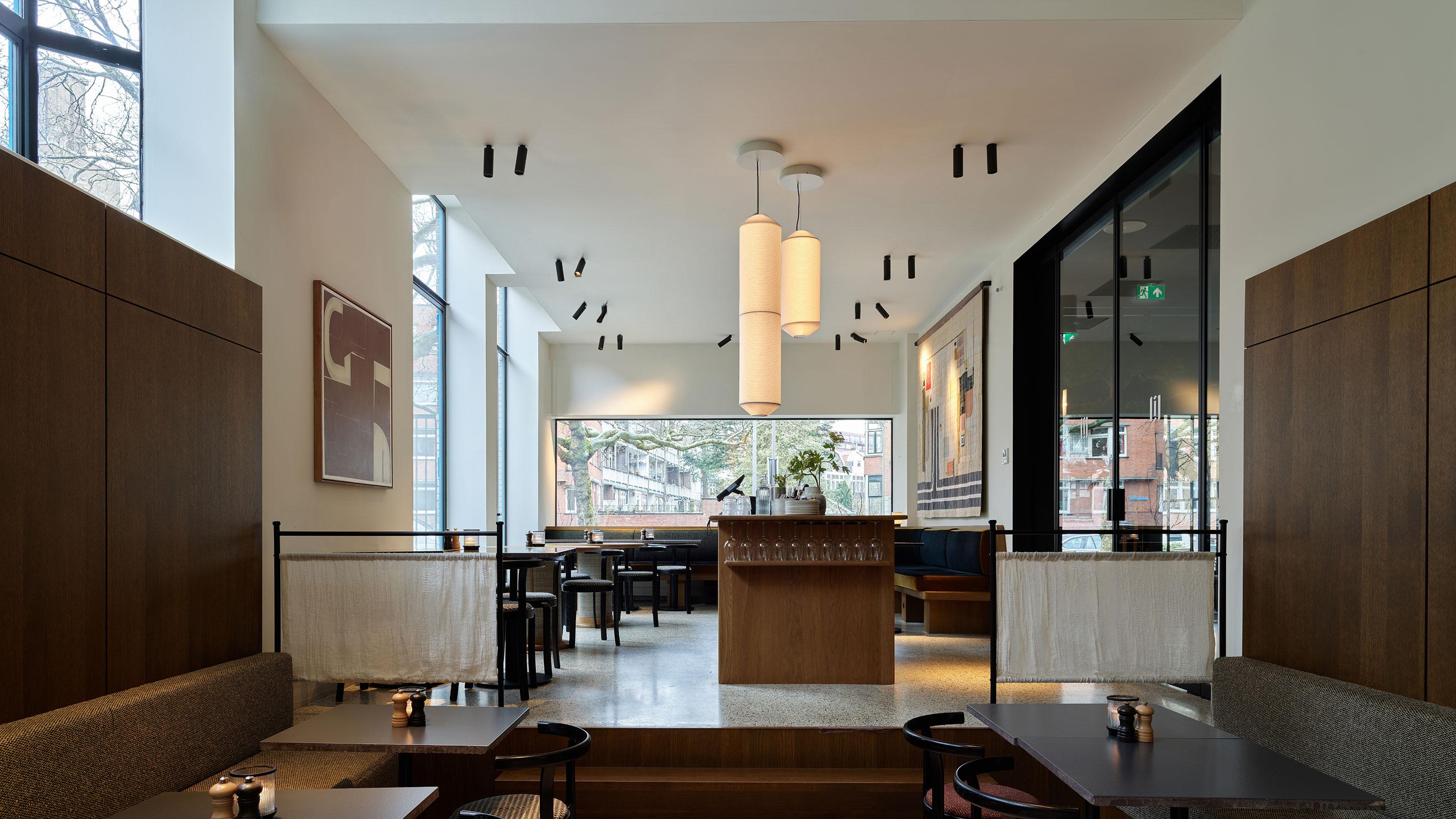 Modern restaurantinterieur met een naadloos akoestisch plafond, houten accenten, grote ramen en minimalistische verlichting. 