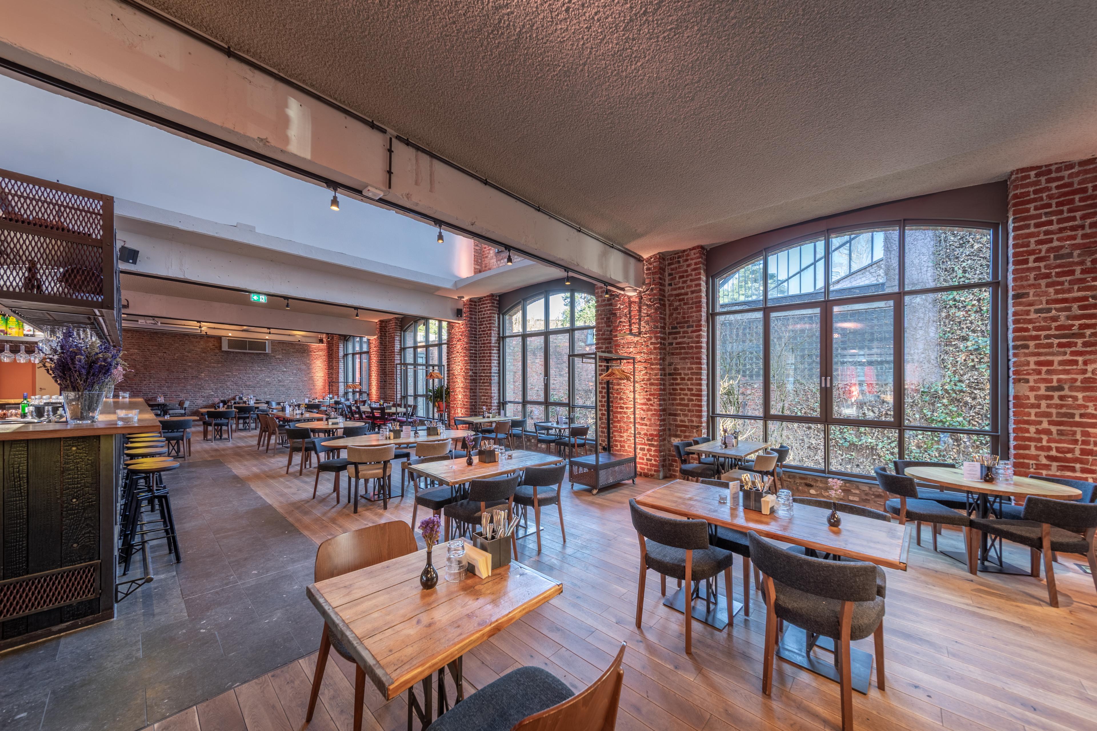 Modern restaurantinterieur met een naadloos akoestisch plafond, houten vloeren, bakstenen muren en grote ramen die natuurlijk licht binnenlaten. 
